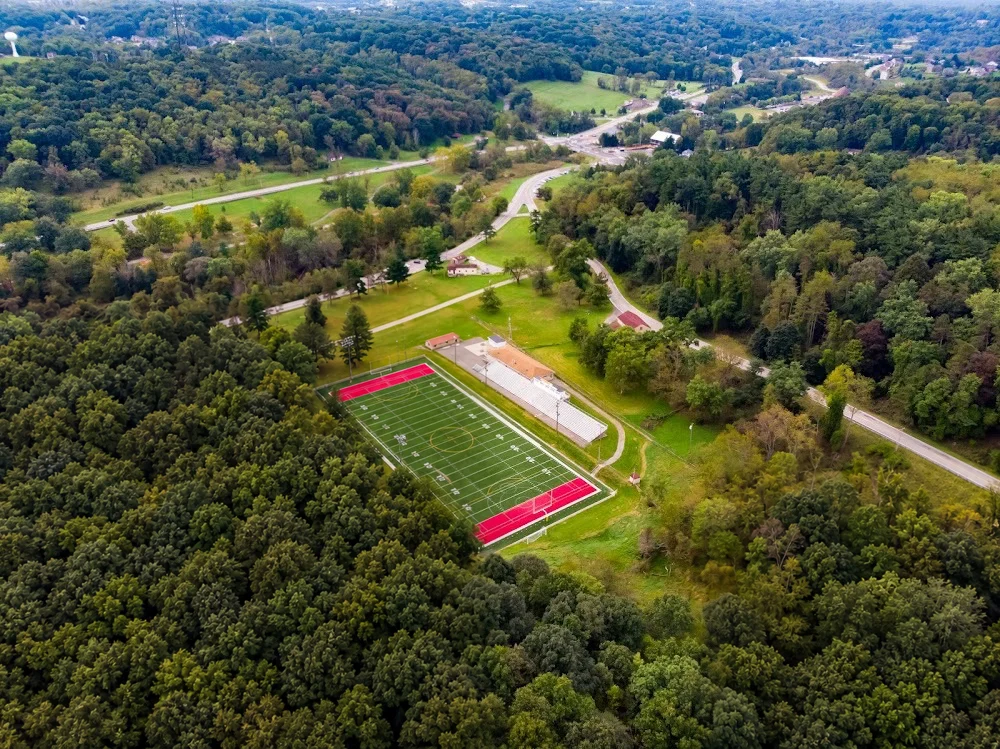 Aerial view of J.C. Stone Field in North Park, showing the turf field, end zones and bleachers surrounded by woods